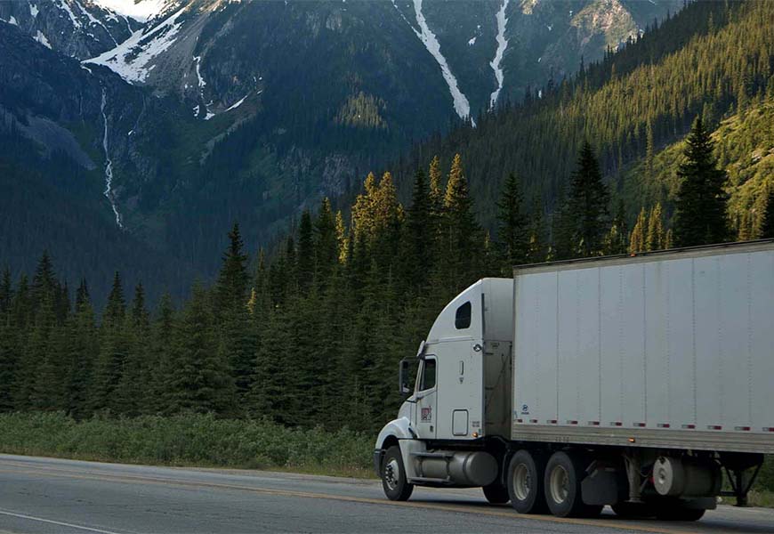 Keystone A white semi-truck equipped with Keystone Alternators drives through a mountainous landscape, surrounded by evergreen trees and snow-capped peaks. Alternators & Starters